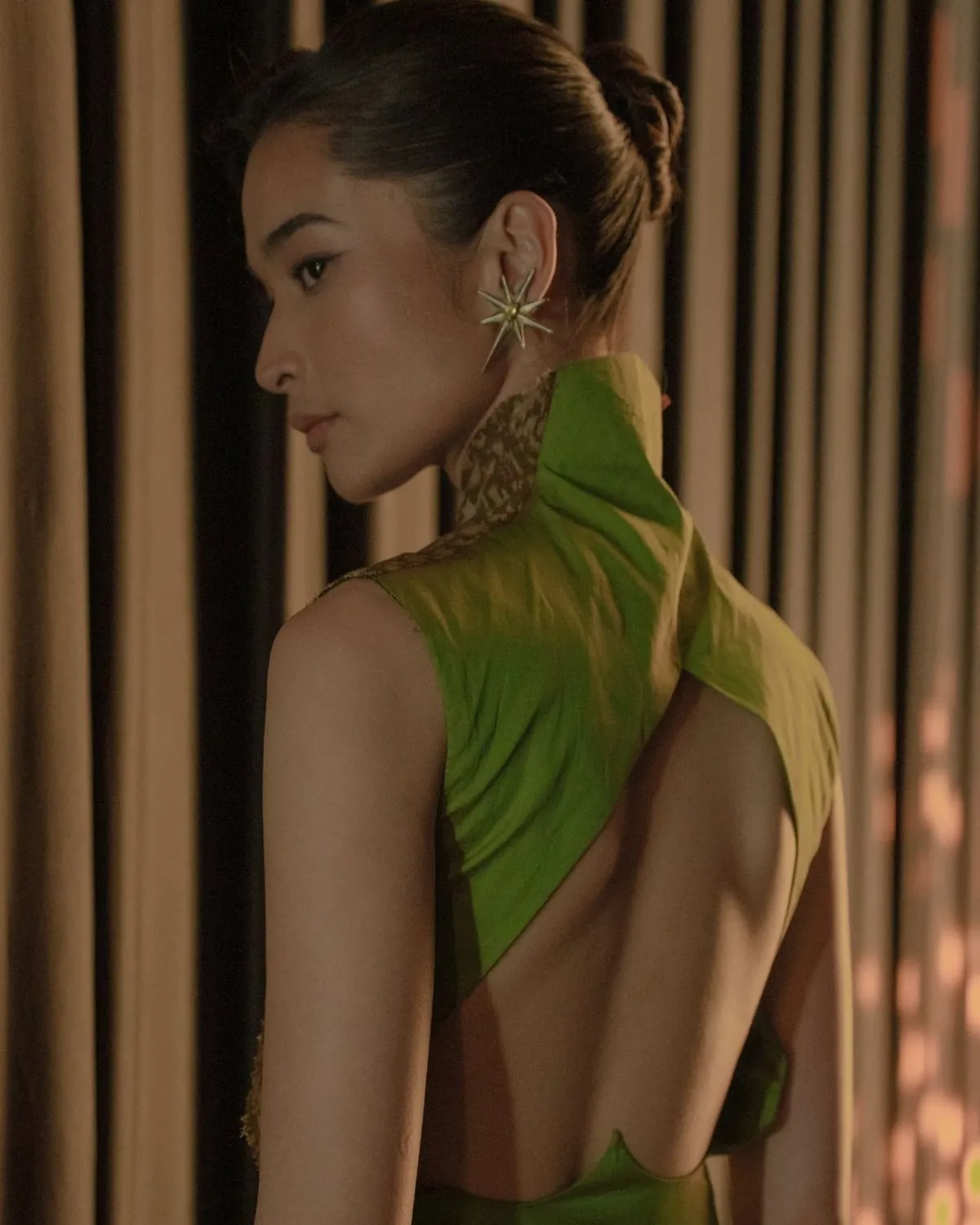 Model seen from behind in a chartreuse backless dress with a high collar trimmed in gold woven textile.