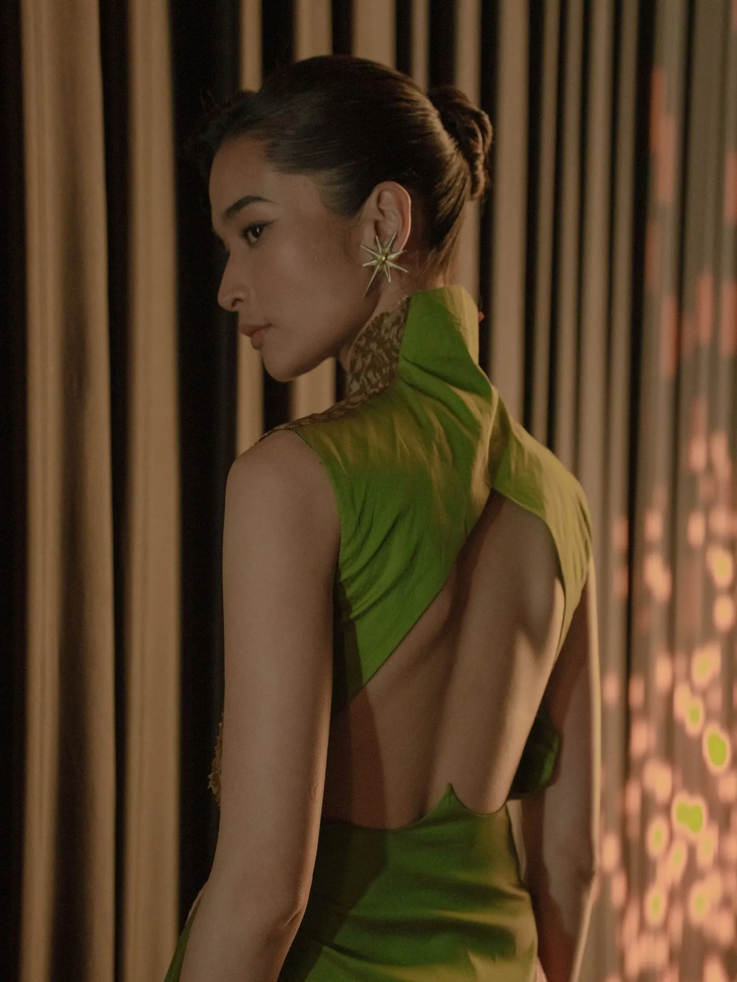 A model seen from behind in a chartreuse backless dress with a gold woven high collar.