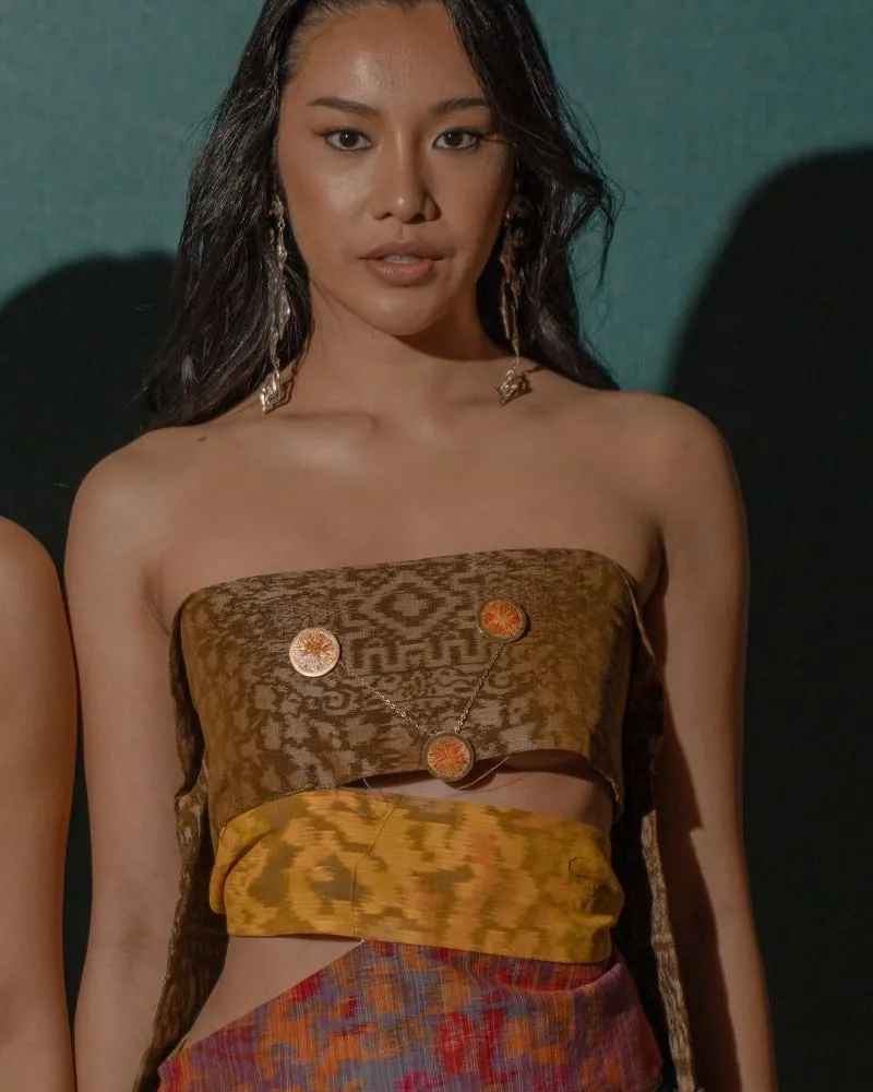 Model wearing a structured bustier in patterned brown tenun with statement buttons and a cut-out ikat waistband.