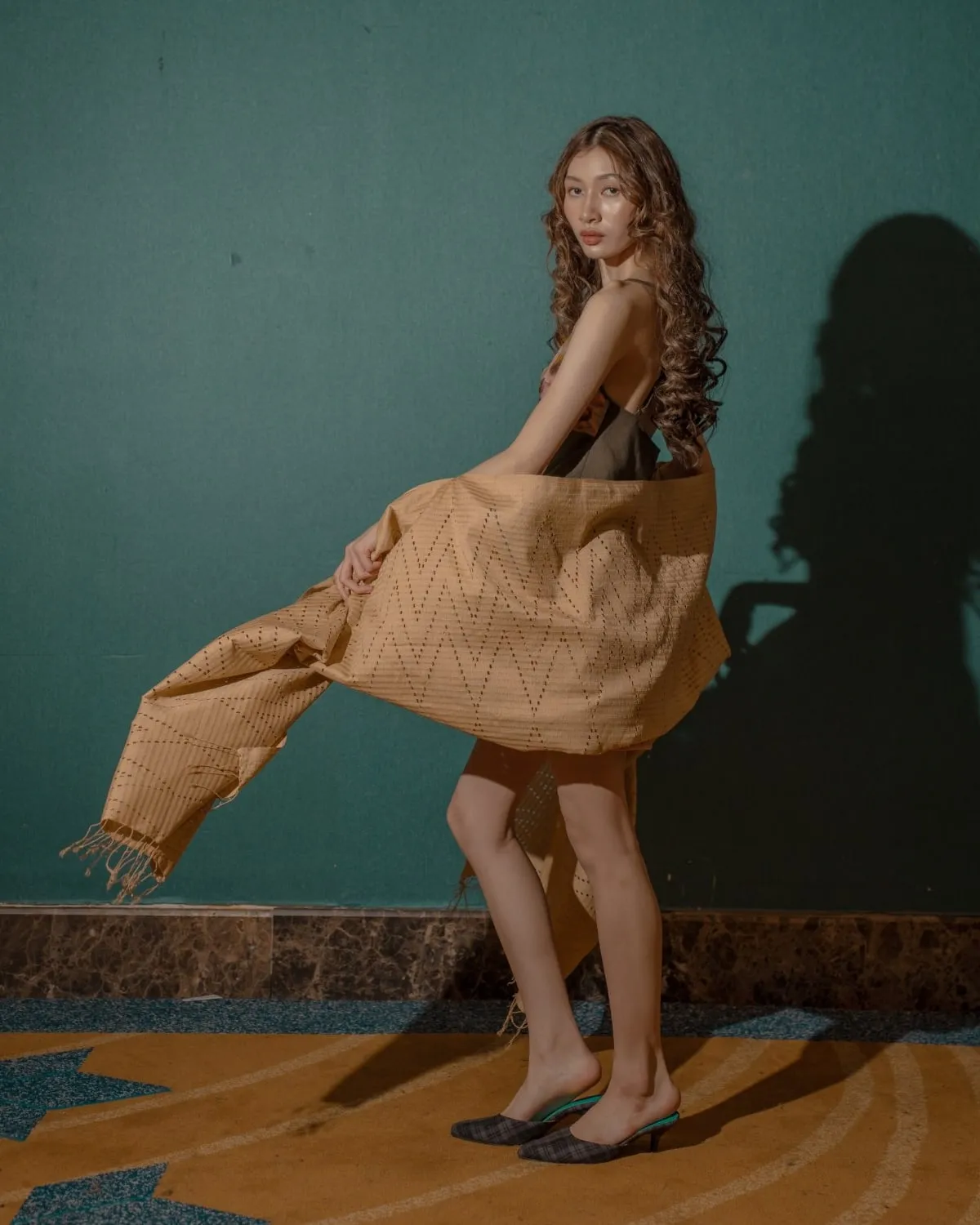 Model turning as a sand-coloured woven shawl with a zigzag pattern flows around her.